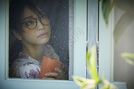 透过窗户看下雨的年轻女人图片