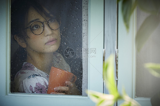 透过窗户看下雨的年轻女人图片