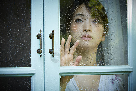 透过窗户看下雨的年轻女人图片