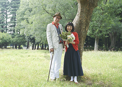 手捧鲜花站在树下的夫妻二人图片