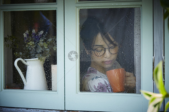 下雨天站在窗户前发呆的孤独女性图片