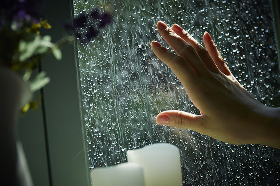 下雨天站在窗户前发呆的孤独女性的手部特写图片