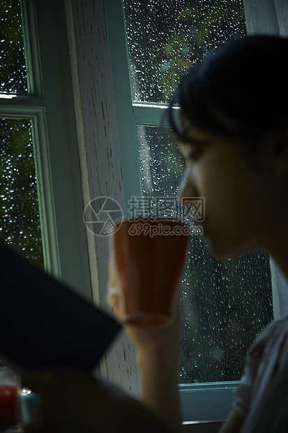 下雨天站在窗户前发呆的孤独女性图片