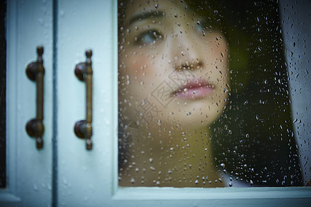 下雨天站在窗户前发呆的孤独女性图片