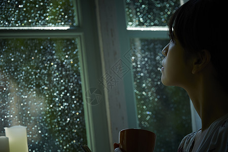 下雨天站在窗户前发呆的孤独女性图片