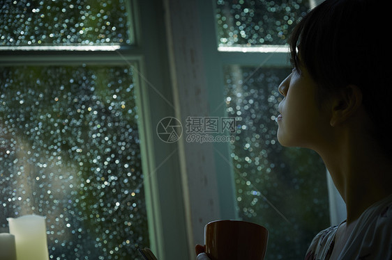 下雨天站在窗户前发呆的孤独女性图片