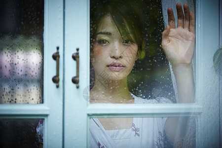 下雨天靠在窗边发呆的孤独女性背景图片