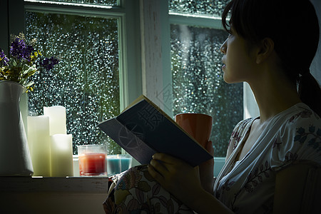 雨夜拿着书本坐在窗边的女孩图片