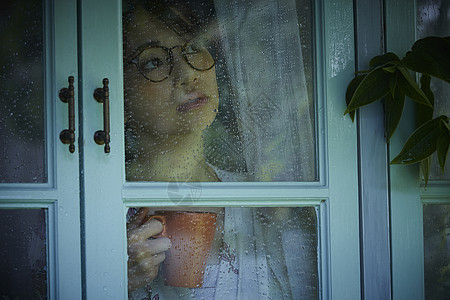 下雨天看向窗外的年轻女性图片