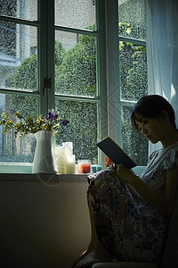 下雨天坐在窗边阅读的年轻女性图片