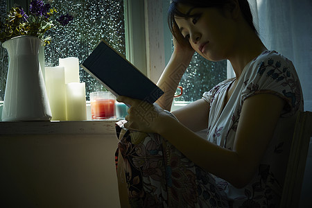 下雨天坐在窗边阅读休息的年轻女性图片