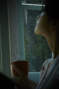下雨天居家拿着水杯看向窗外的女性图片