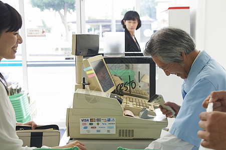 便利店为顾客结账的老年店员图片