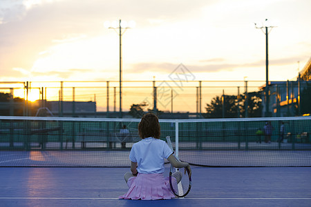 夕阳下坐在网球场的女人背影图片