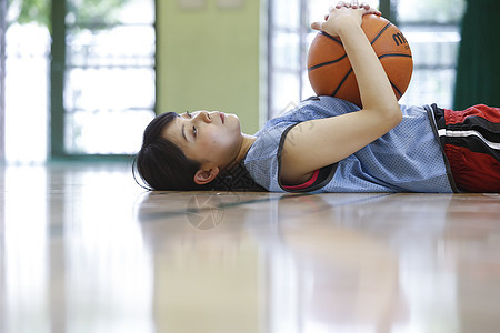 抱着篮球躺在篮球场上的年轻女性图片