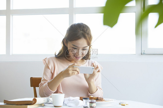 餐桌上拿着手机拍照片的女性图片