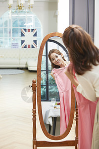 站在镜子前拿着粉裙子的年轻女性图片