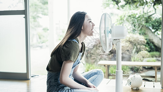 坐在风扇前乘凉的美女背景图片