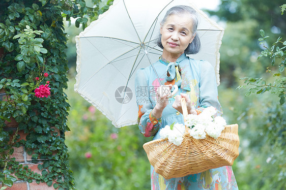 爱好60几岁愉快拿着遮阳伞的资深妇女在庭院里图片