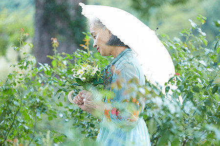 一个男人掌握植物人拿着遮阳伞的资深妇女在庭院里图片