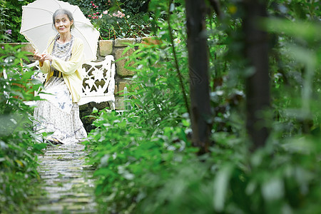拿着遮阳伞坐在庭院里的老妇人图片
