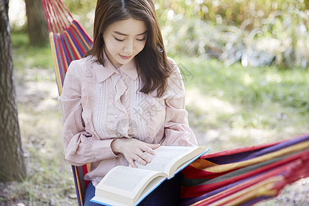 看书的女子坐在户外吊床上阅读的女青年背景