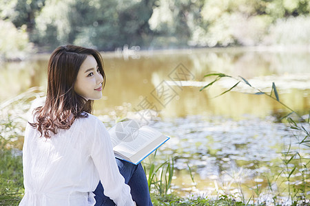 坐在河岸边阅读的女青年图片