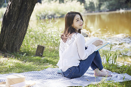 坐在河岸边阅读的年轻女子图片