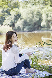 公园坐在河岸边阅读的年轻女子图片