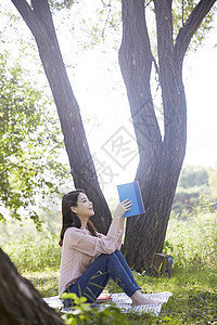 公园郊游拿着书籍阅读的年轻女性图片