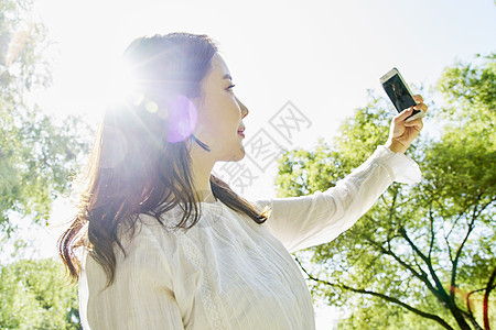 公园里拿着手机自拍的女性图片