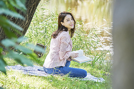年轻女子坐在公园小河边阅读图片
