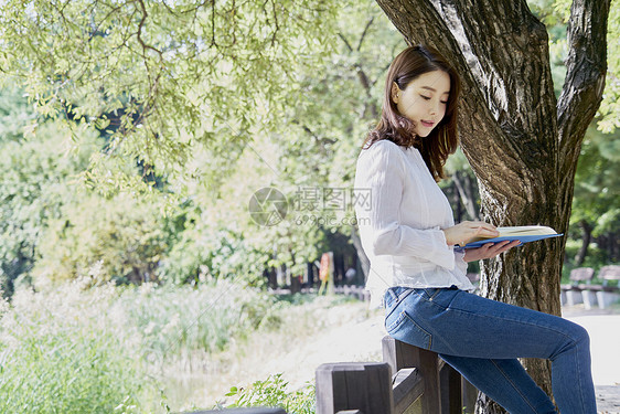 坐在公园栏杆上阅读的年轻女子图片