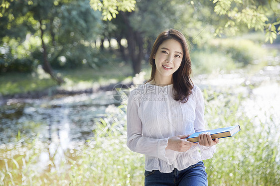 公园里拿着书的年轻女大学生图片