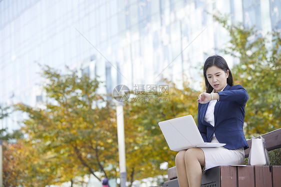 坐在长凳上看手表焦急的女性图片