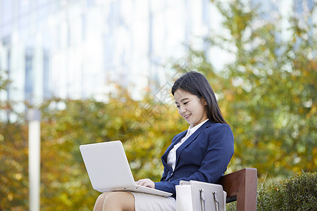 坐在长凳上使用笔记本电脑的女性图片