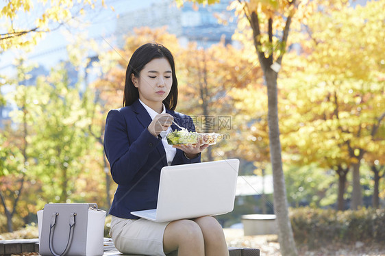 坐在长凳上吃沙拉的女青年图片