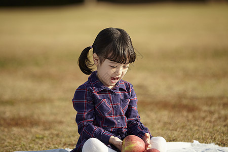 坐在野餐垫上的小女孩抱着苹果图片
