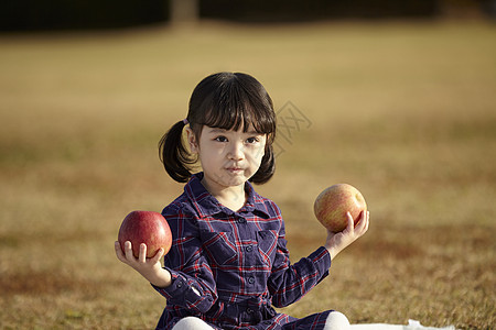 坐在野餐垫上的小女孩抱着苹果图片