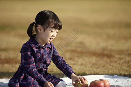 坐在野餐垫上的小女孩抱着苹果图片