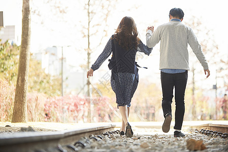 公园情侣牵手年轻情侣户外公园约会牵手散步背影背景