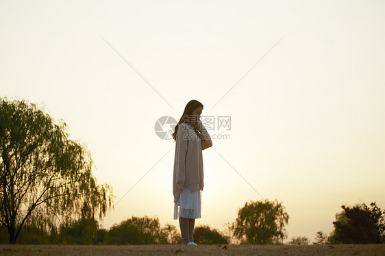 夕阳下站在公园草坪上的女性图片