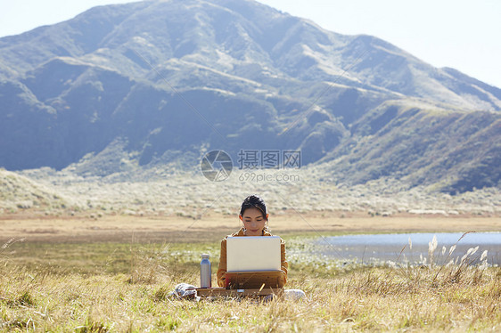 带着便携电脑旅行在草地上工作的女人图片