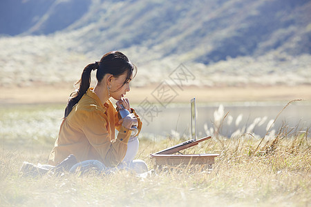 带着便携电脑旅行在草地上工作的女人图片