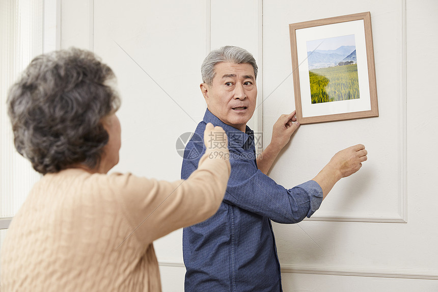 老年夫妻在墙上挂相框图片