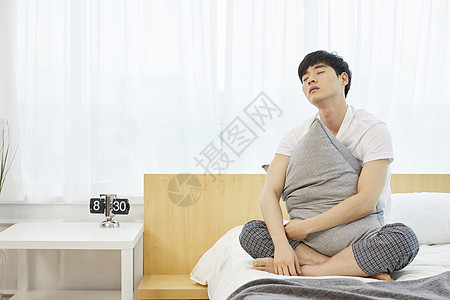时钟起床抱着枕头疲惫的男青年背景