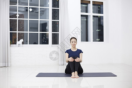 青年女子抱腿屈膝坐在瑜伽垫上图片