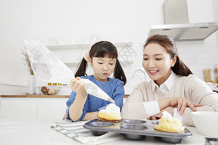 母亲微笑的看着挤奶油的小女儿图片