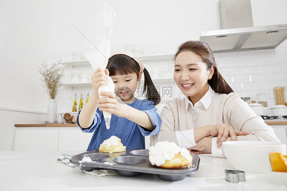 母亲微笑的看着女儿挤奶油做甜品图片
