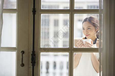 站在窗外捧着咖啡的女青年图片